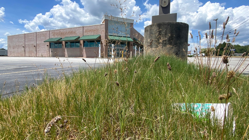 Macon: Grass growing around empty parking lot around closed large building.