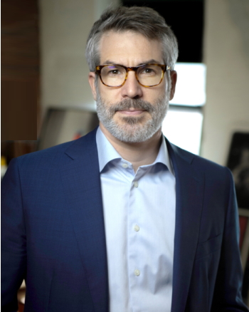 Macon: Serious-looking man with graying hair, mustache, beard, wearing glasses, dark blue jacket, light blue shirt.