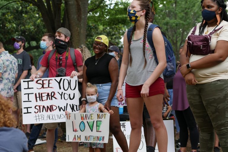 defunding: People in masks, including little girl, stand still, hold up signs