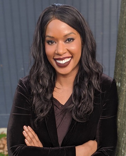 April Goodwin headshot smiling woman with long dark hair and with arms crossed weaaring black suit