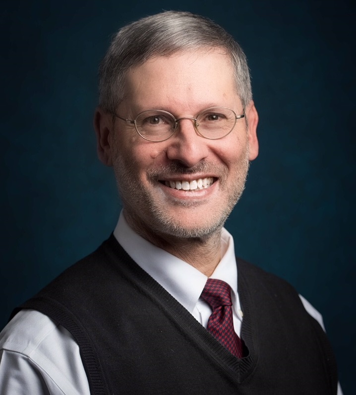 alt text: peer-on-peer: Daniel Pollack (headshot), Yeshiva University professor; smiling man with beard, mustache, glasses wearing blue tie, white shirt, dark vest.