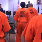 South Carolina: Men standing seen from the back wearing orange uniforms with scdc inmate on back.