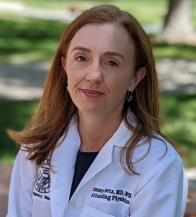firearm injuries: Emmy Betz (headshot), emergency physician, researcher at University of Colorado School of Medicine, woman with long red hair in doctor’s white coat with name on it