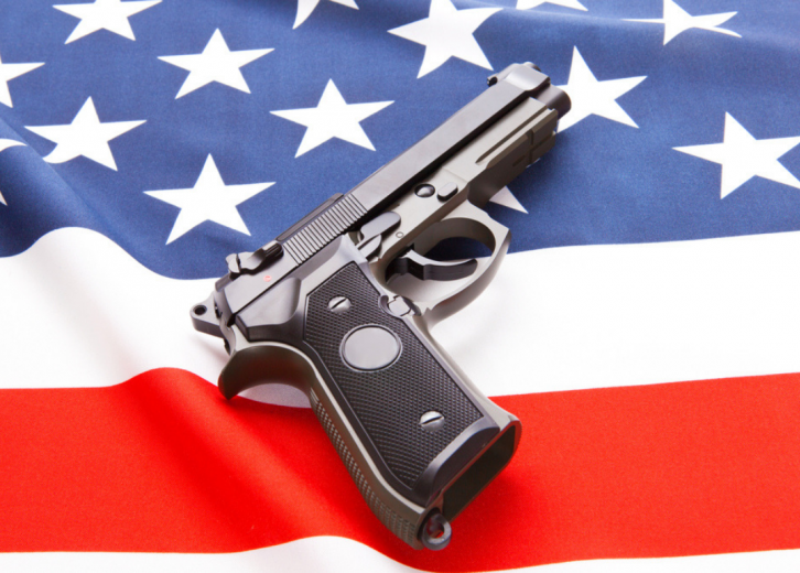 handgun on closeyop of partial blue star field andred/white stirpesof an American flag.