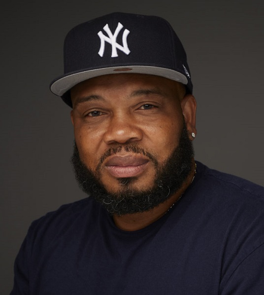 Omar Jackson (headshot), director of Stand Against Violence East Harlem, man with beard, mustache wearing Yankees cap and dark blue T-shirt