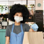 COVID-19: Food worker wearing face mask and gloves holding takeout order in bag.