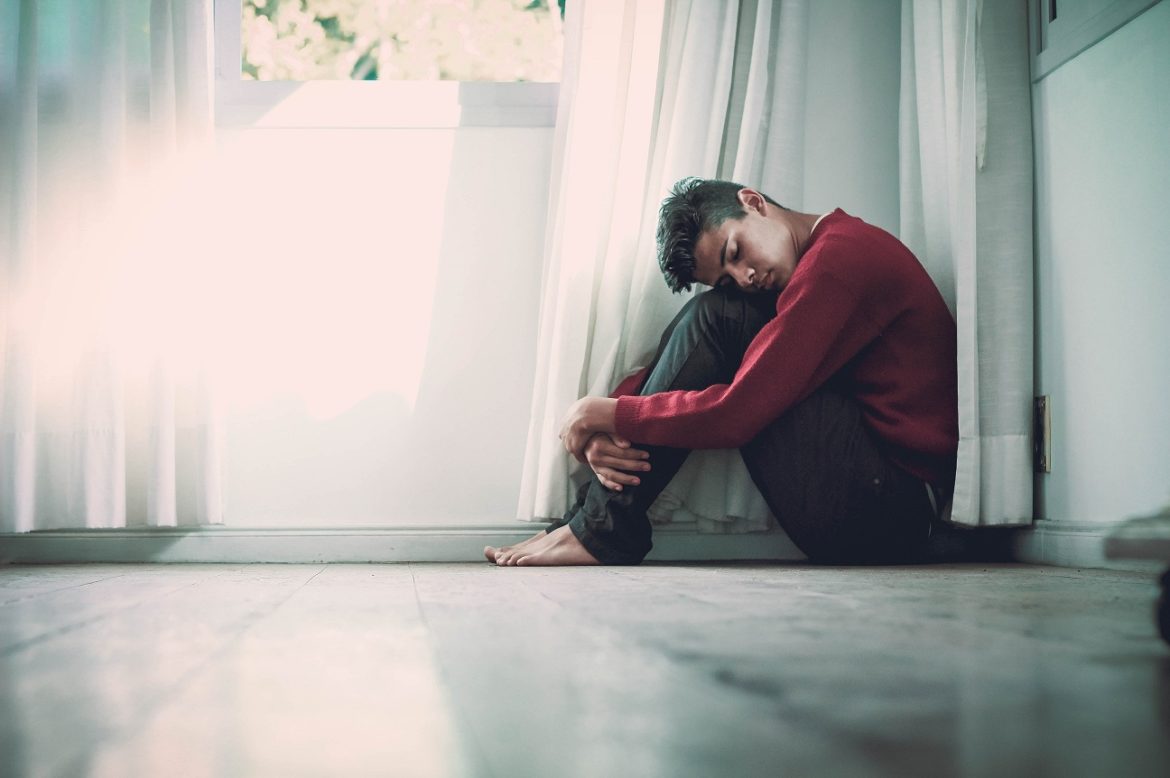 suicide: Youth sitting on floor next to curtain, head on knees