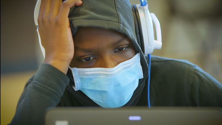 homeless: Close-up of student in mask, hoodie, headphones leans over laptop