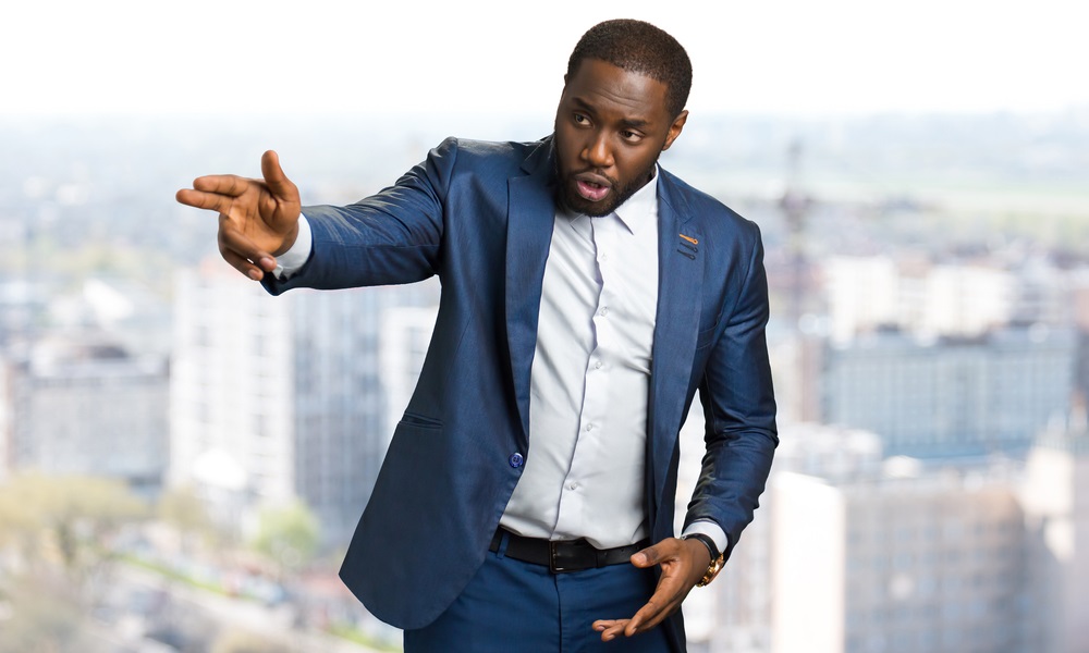 Man of color in business suit pointing to left against background of city