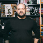 Extremism: Christian Picciolini, Balding man with dark hair, beard, mustache, black top stands in front of bookshelves