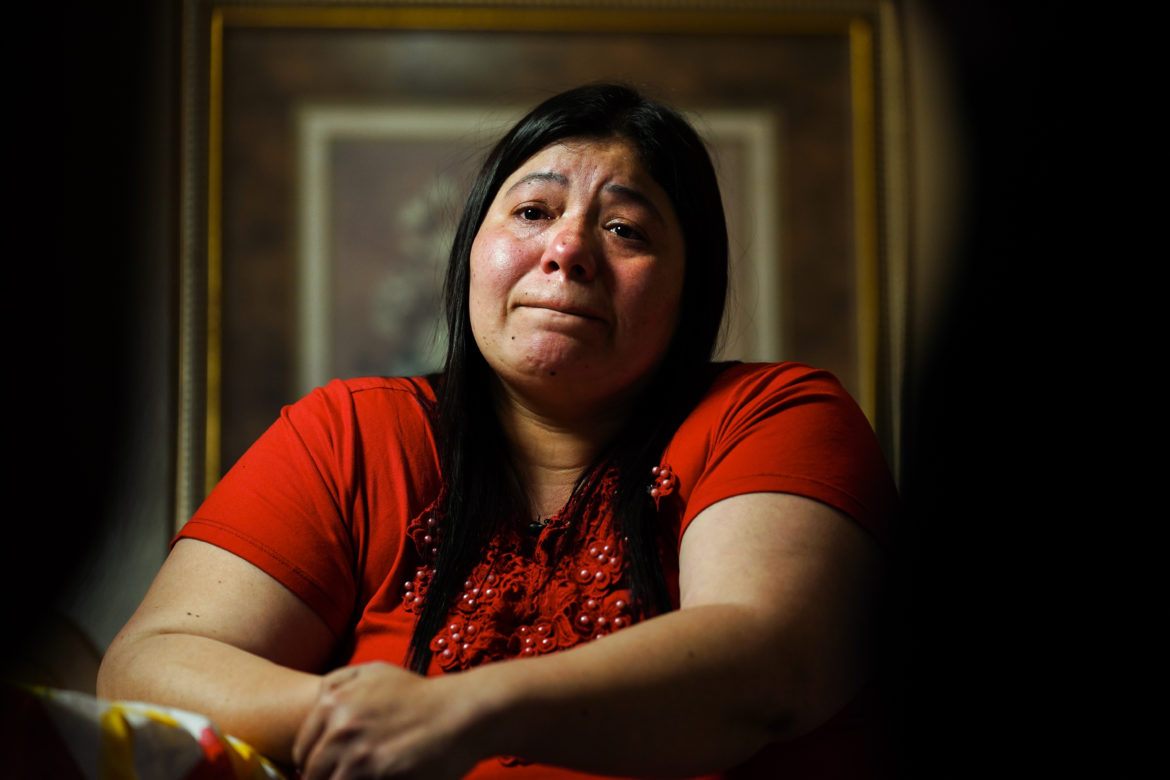 Immigrant children left at border: Woman with long, dark hair in red top sits at table crying with hands folded on table.