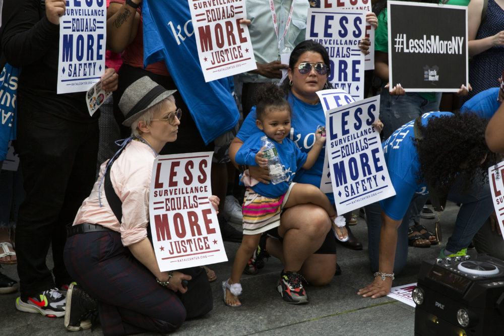 #LessIsMore Rally NY: Several people holding Less Is More signs stand and sit on sidewalk