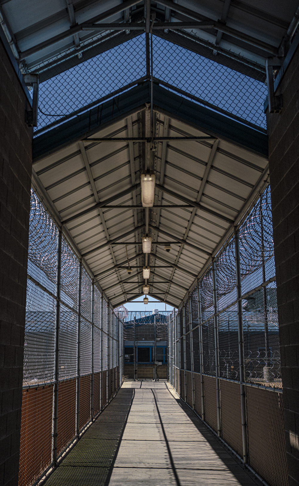 New Mexico jail: Long, outdoor cement sidewalk completely enclosed with chain link fence topped by barbed wire that meets the peaked metal roof