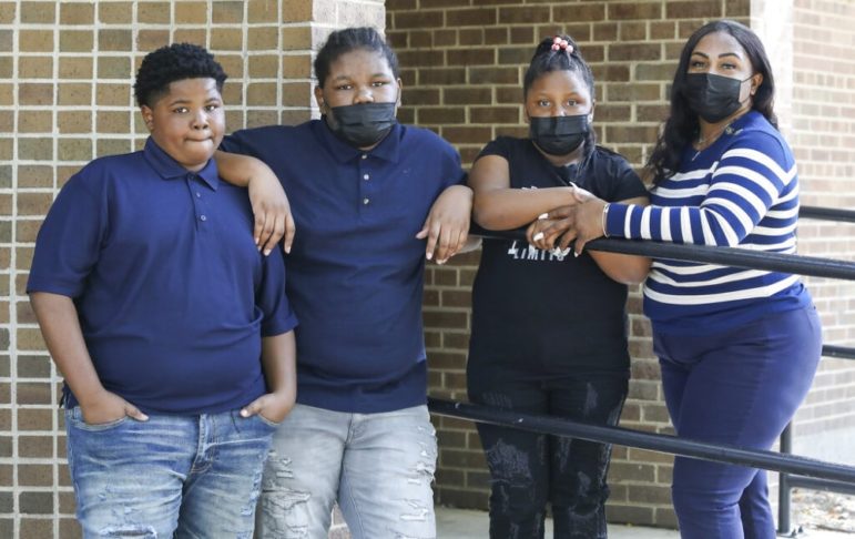 Police excessive force children: group of young black kids standing with masks on near railing and brick building