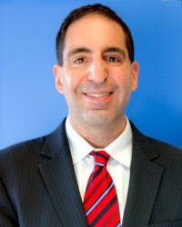 Eric Solomon headshot: man with dark hair in suit and red tie on blue background