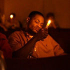 Accidental drug overdose: Black man wearing tan shirt sits holding lit candle in dark room