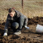 Teen facilities: Young teen crouches in garden bed wearing heavy overcoat and garden gloves prepping soil.