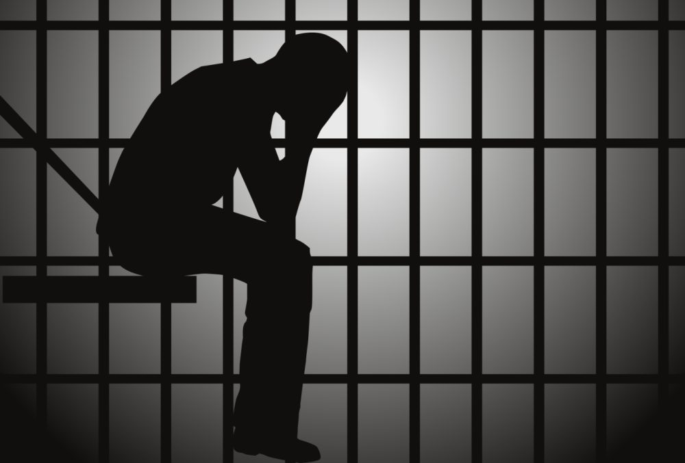 Juvenile detention rough in La. illustration of persn's silhouette sitting with head in hands in jail cell