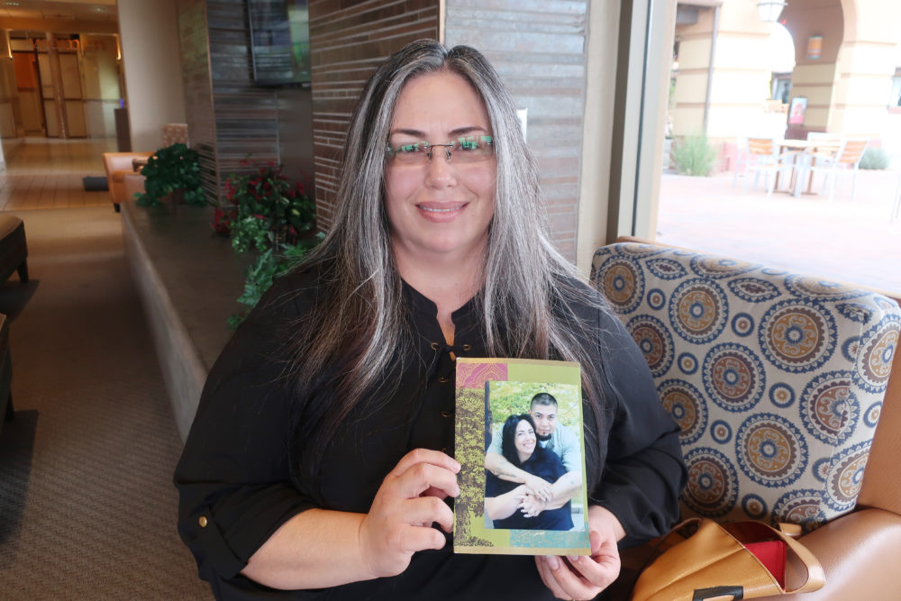 Juvenile lifers: Middle-aged woman with long dark, graying hair wearing black top stands holding collaged photo of her younger self with a young, dark-haired mn hugging her from the back