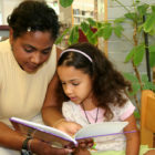 Children incarcerees: Black adult woman sits reading book to younf black girl sitting next her
