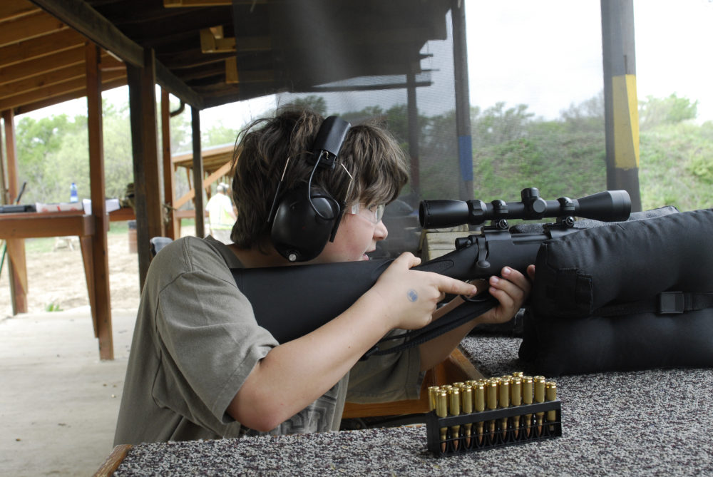 rural youth and handguns: Boy with sound-muffling head phones holds and shoots a rifle at a range.