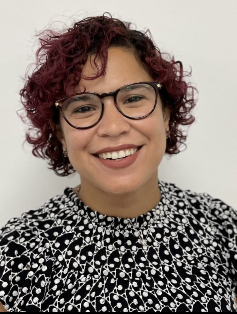 LGBTQ juvenile justice: Headshot of woman with sort, curly auburn hair with darkframed glasses wearing a black and white print top.
