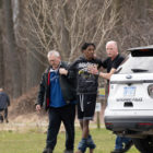 Juvenile Sentencing: Two policeman holding Black male teen between them walt around whote police car in a grassy park
