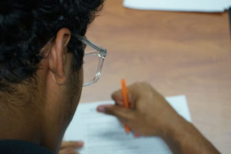 Utah College Classes: Dark-haired person with glasses and orangepen writes on a white paper