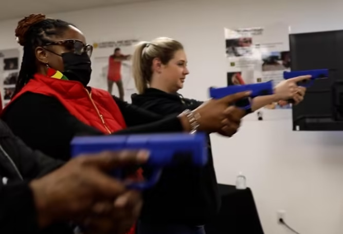 Girls and Guns study: Twi young women aim blie practive anduns at a taregt in an indoor gun training class
