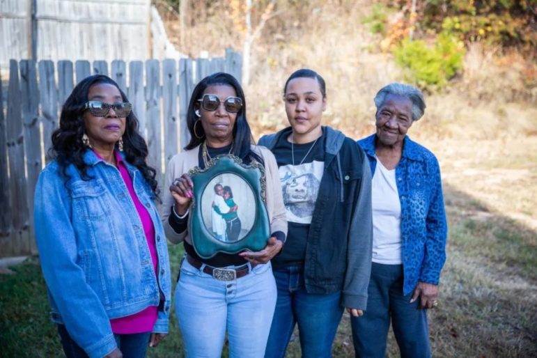 toll of his absence; women supporting prisoner Almeer Nance: four woman standing in yard with one holding an old framed picture
