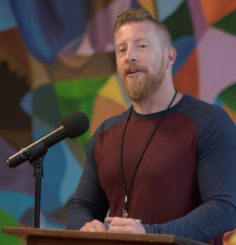 Teen Murder Sentence: White man with red hair and beard in dark, long-sleeved t-shirt stands behind podium speaking into microphone