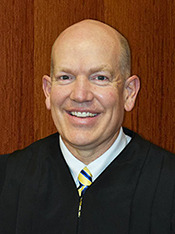 Drug Court: Headshot of bald man wearing black judge's robe smiles into camera