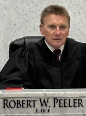 Drug Court: Man with short browb hair wearing a black judge's robe sits inside a gray marble judges bench