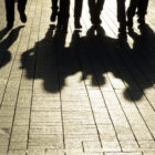 No Place for Kids; Silhouette of feet and legs abd their full body shadows of four people in cobblestone walkway