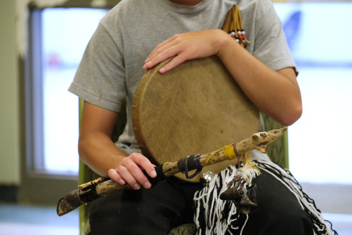 Native American rituals: Closeup of person's chest and arms in tan t-shirt holding a stick with several feather's attached