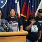 Uvalde families plead for languishing Texas gun bills: group of people in black shirts stand next to someone speaking at podium