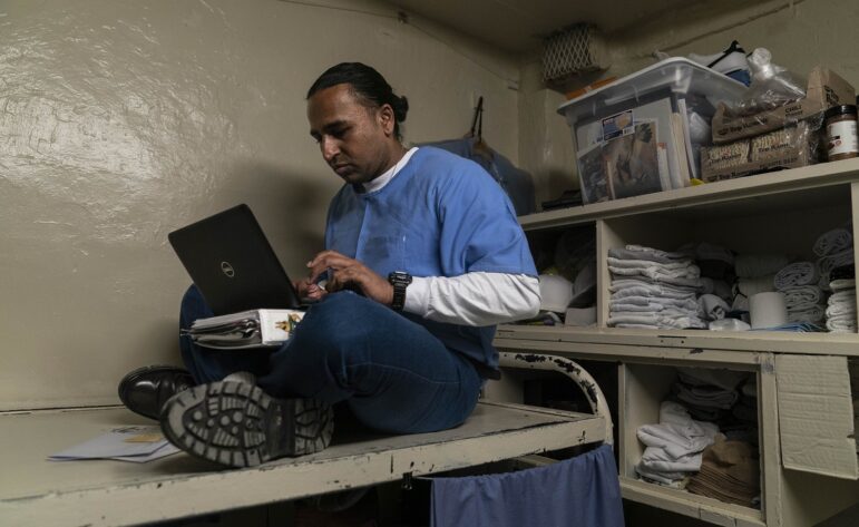 Free college for more prisoners: man in blue shirt sits on prison bed working on laptop