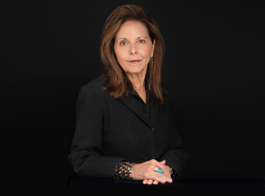 Juvenile justice reform: Katherine Lucero headshot woman with long, brown hair in black blouses sits with hands folded in front of black background
