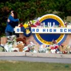 school shooting: Oxford high school sign covered in flowers and memorial items while two people hug