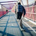 First-time juvenile offenders: Teen skateboarder in jeans and blue plaid shirt speeds through the pedestrian walkway on paved road over red metal bridge