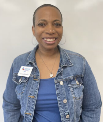 School shooting counselor: Headshot of Black woman with bald head in blue denim jean jacket and blue top smiling into camera