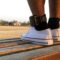 Juvenile diversion and probation: Closeup of two feet wearing white tennis shoes and black socks with an ankle monitor on left ankle