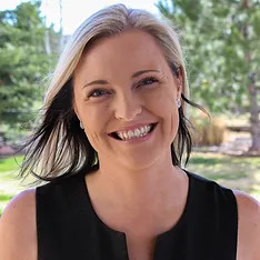 Trauma-informed teaching: Headshot Heather Martin, woman with blonde hair in long bob, wearing black sleeveless top, smiling into camera with green trees in background