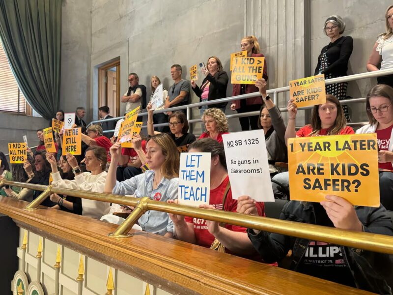 Tennessee arms teachers: Several adults stand and sit in balcony gallery area, many holding signs with language protesting arming teachers in schools