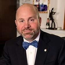 Cayuhoga juvenile defenders: MIDDLE-AGED BALDING MAN WITH SHORT BROWN BEARD IN BLACK SUIT, WHITE SHIRT AND DARK BLUE BOW TIE