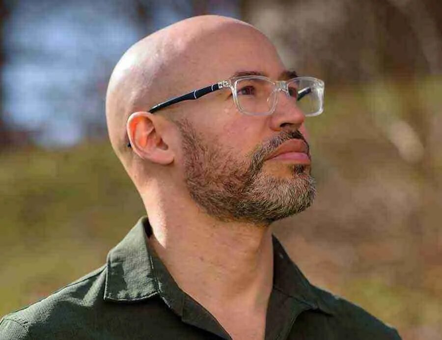 Restorative justice manual: Headshot Felix B. Rosado. Bald man with short, dark graying beard and clear plastic glasses wearing dark shirt in 3/4 profile looking up.