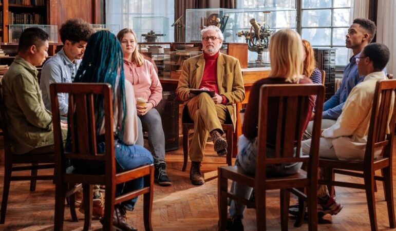 Restorative justice: Group of adults and teens sit in dark wood library in dark wooden chairs in a circle