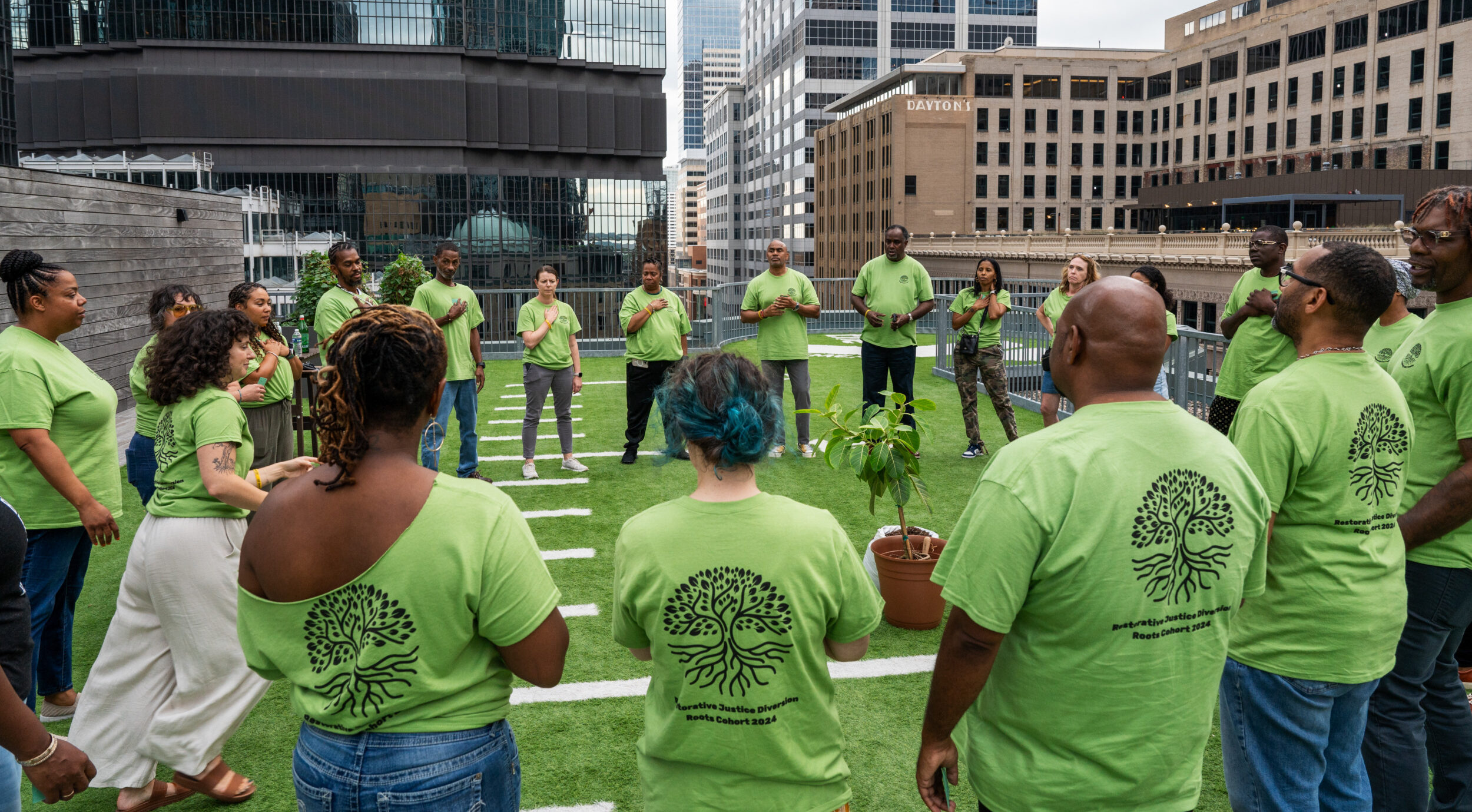 Restorative justice partnerships: Group of around 20 people stand in a circle on artificial turf field surrounded by tall city buildings