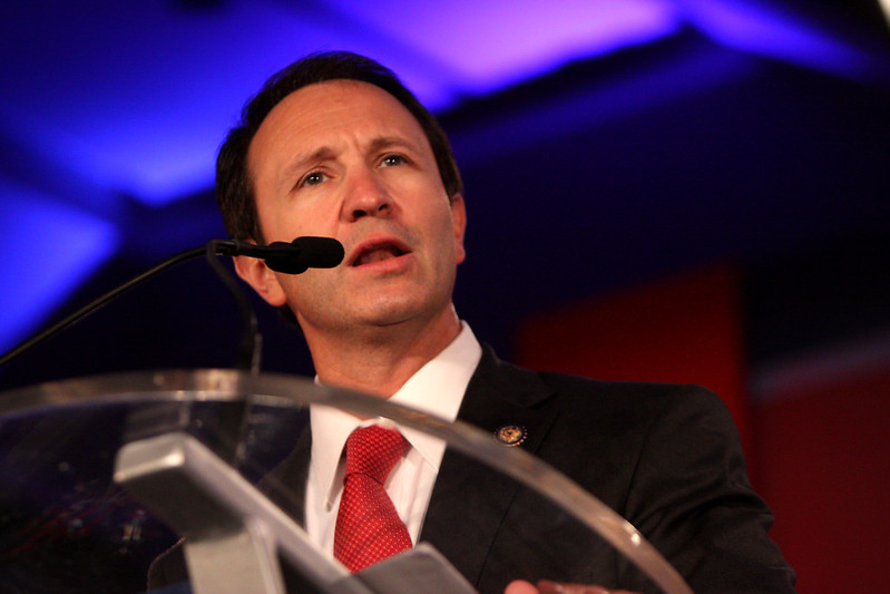 Teens adult prison: Man with short dark hair in navy suit, white shirt and red tie, speaks into microphone on podium